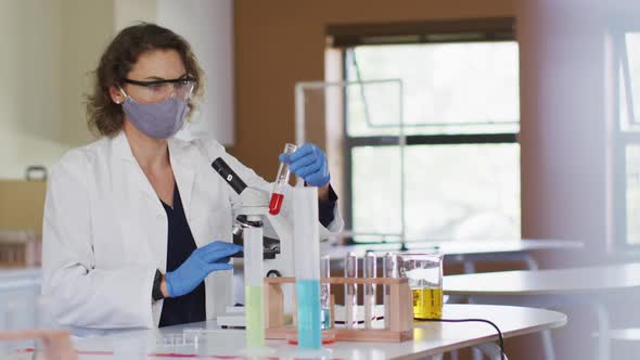 Female teacher wearing face mask holding test tube at laboratory at school