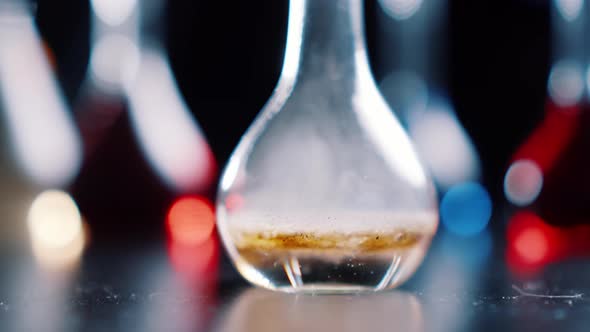 Stormy chemical reaction in laboratory flask with boiling and foaming. Table with medical bulbs