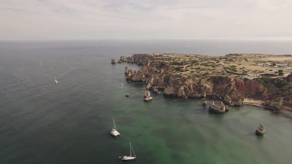 Summer paradise Lagos coastline, natural rock formation and sailboat sailing on tranquil ocean.