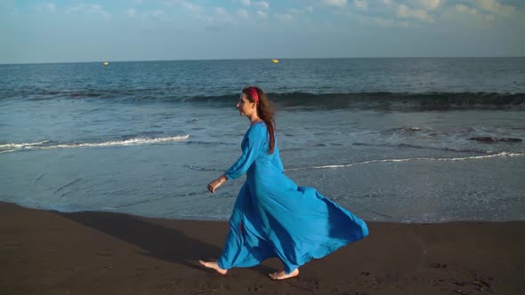 Woman in Beautiful Blue Dress Walking Along a Black Volcanic Beach