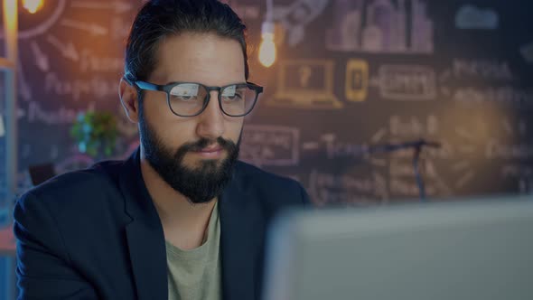 Attractive Middle Eastern Man Using Computer in Dark Office Concentrated on Online Work