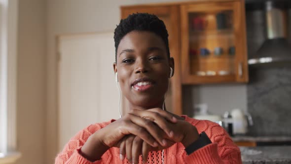 Portrait of african american woman wearing earphones talking looking at the camera at home