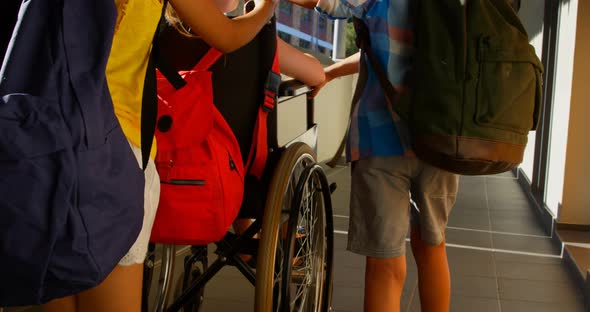 Schoolkids pushing disabled schoolgirl in wheelchair at corridor 4k