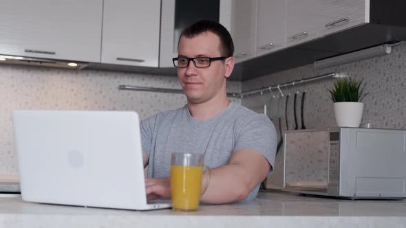 Young Male Freelancer Uses a Laptop While Working From Home on the Internet Looking at the Screen