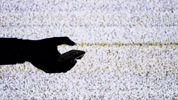 Silhouette of a Hand Holding a TV Remote on TV Screen Background with White Static Noise