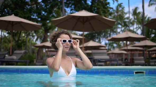 Caucasian Woman in a White Swimsuit and Wears Her Sunglasses While Standing in a Swimming Pool