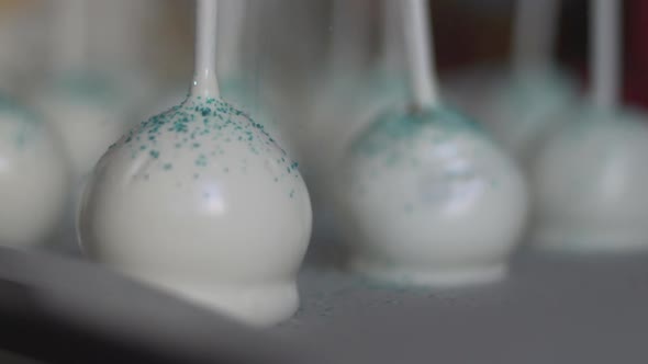 Close up of white cake pops, edible pastry glitter falling on them, slow motion 120fps