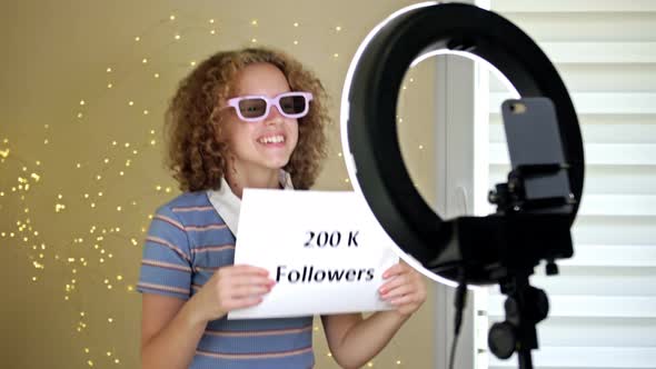 Cheerful Girl Blogger Shows a Poster with 200 Thousand Subscribers to the Camera