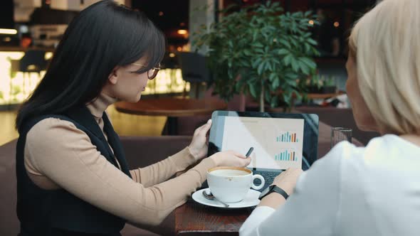 Businesswomen Talking in Cafe Discussing Cooperation Pointing at Laptop Screen