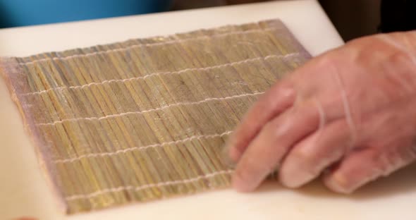 Chef Puts Seaweed Wrap And Sushi Rice On A Bamboo Mat For Rolling - close up, slow motion