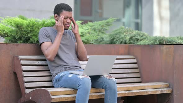 Young Young African Man with Laptop Having Headache on Bench 