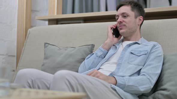 Young Man Sitting on Sofa and Talking on Smartphone 