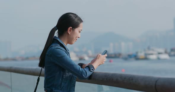 Woman use of mobile phone and standing at the seaside bay