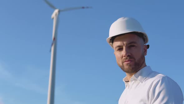 Portrait of a Man in a White Helmet and a Classic Shirt on the Background of a Wind Turbine of a