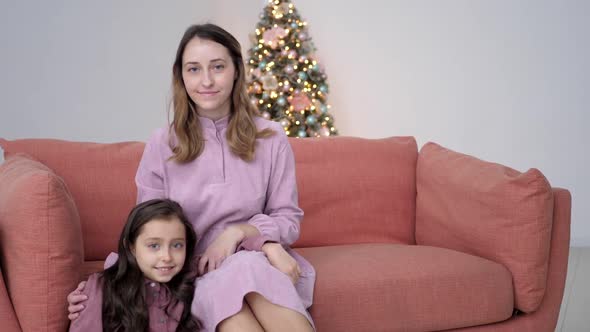 Mom and Daughter in Purple Dresses Sitting on Couch at Home on Christmas Day