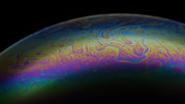 Close-up of soap bubble. Multicolored rainbow iris like colorful gas planet on black background