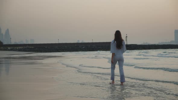 Back View of Brunette Woman Walking in Water with Skyline of Dubai Skyscrapers in the Background