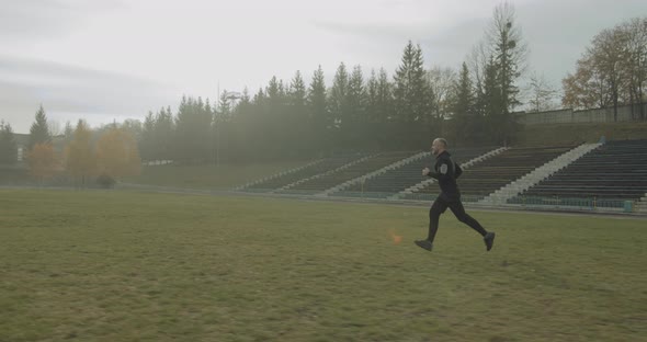 Athlete Is Running Across the Stadium Field in the Morning in Foggy Autumn Weather 