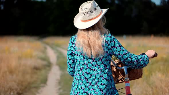 Girl Relaxing On Countryside Wildflower Field.Girl In Hat Enjoying Weekend.Cyclist Walking With Bike