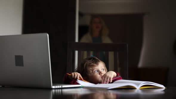 Little boy play with notebook, stickers and parents laptop at table at home
