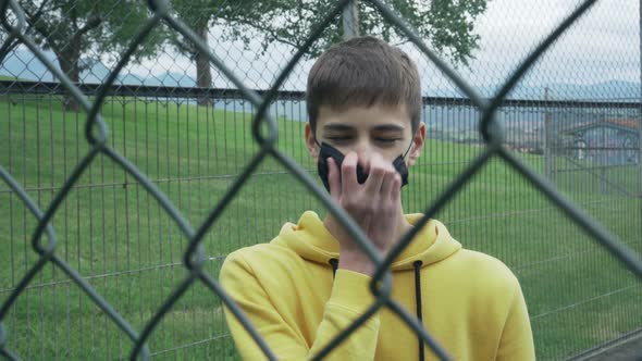 Young man rips off a medical black mask behind an iron wire fence.