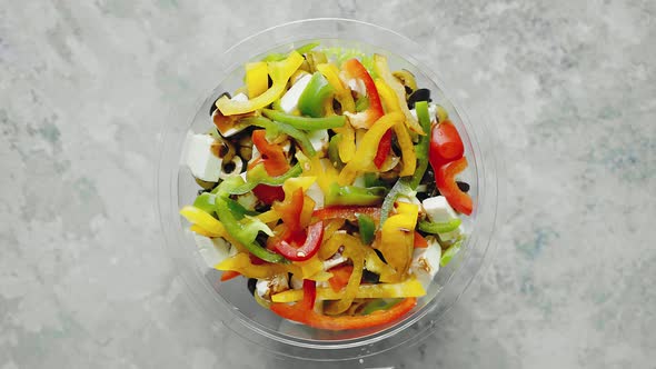 Fresh Greek Salad in Plastic Package for Take Away or Food Delivery on a Stone Table