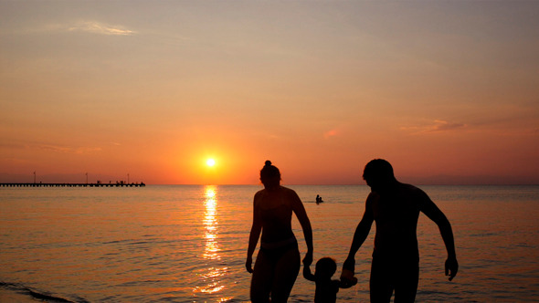 Young Family On The Beach Under A Colourful Sunset