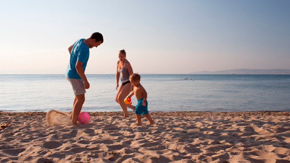 Young Family Playing Football On The Beach