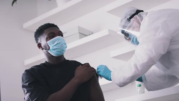 Doctor Wearing a Face Shield Gloves and Mask Giving an Injection to a Guy