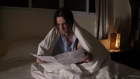 Young Caucasian Lady is Sitting in a Room on a Bed Covered By Blanket and Reading Prescription
