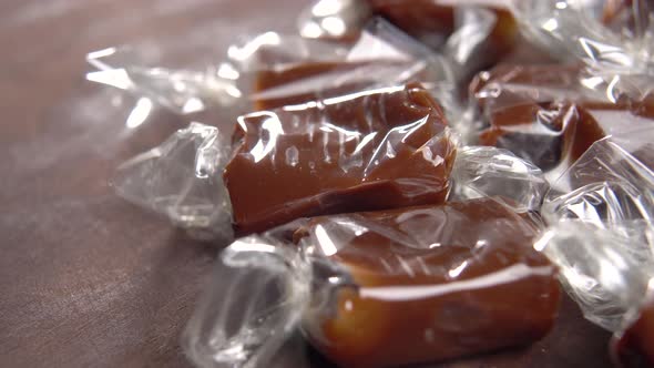 Brown candy toffees in a wrapper on a wooden rustic background. Sweet xmas taffy. Macro