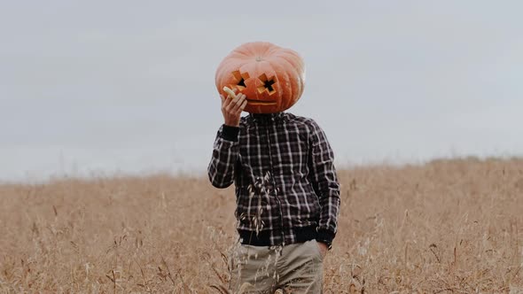 A Funny Man with a Big Pumpkin Head Holds a Candle in His Hand and Pretends to Smoke