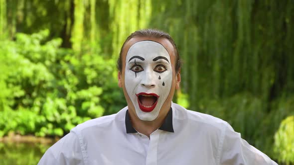 Close-up of a Mime Looking at the Camera Enthusiastically on Green Background in a Park. Emotion of