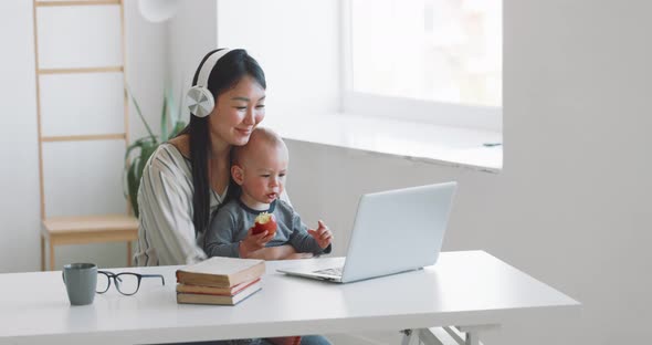 Young Mother Freelancer with Her Child Working at Home Office Using Laptop