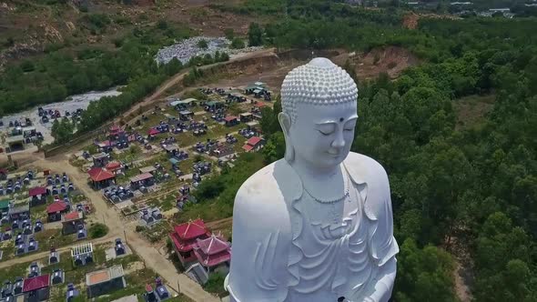 Drone Turns Around White Huge Buddha Statue Against City