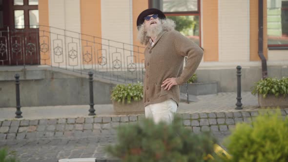 Carefree Relaxed Retiree Strolling Along Town Street with Baggage. Side View Wide Shot of Elegant