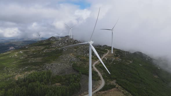 Wind turbines slowly spin on top mountain shrouded in clouds, Caramulo in Portugal. Aerial static vi