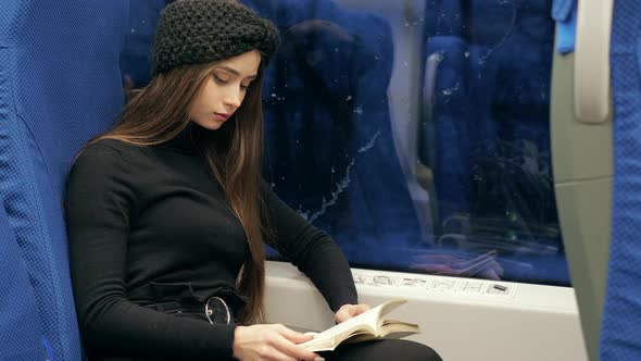 A Woman is Sitting in Public Transport and Reading a Book