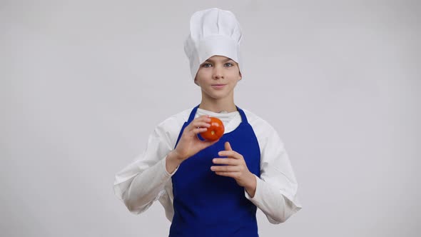 Positive Handsome Caucasian Boy in Chef Uniform Posing Closing Eye with Tomato