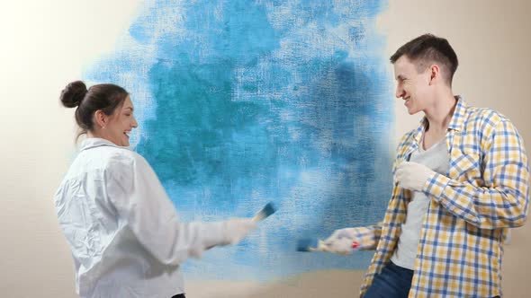 Funny Young Woman and Man in Gloves Fight with Paintbrushes