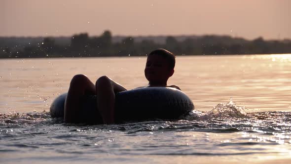 Silhouette of Happy Boy Swiming on Inflatable Circle in the River at Sunset
