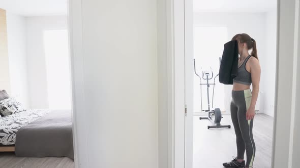 Young woman with towel after training with cross trainer at home