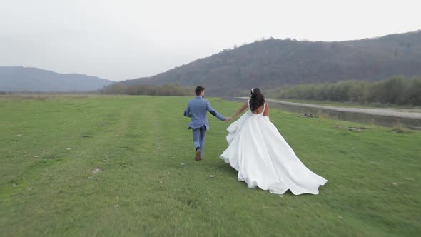 Wedding Couple Running Near Mountain River. Groom and Bride in Love