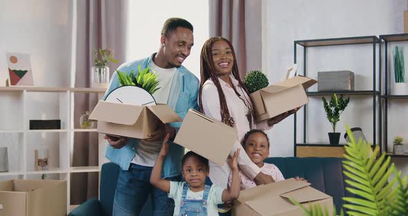 Family with Small Kids Holding Carton Boxes with Home Decor and Looking Into Camera