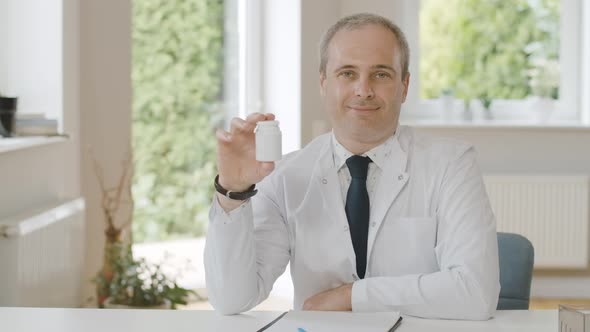 Portrait of Positive Caucasian Doctor Holding Jar with Pills and Smiling at Camera. Professional