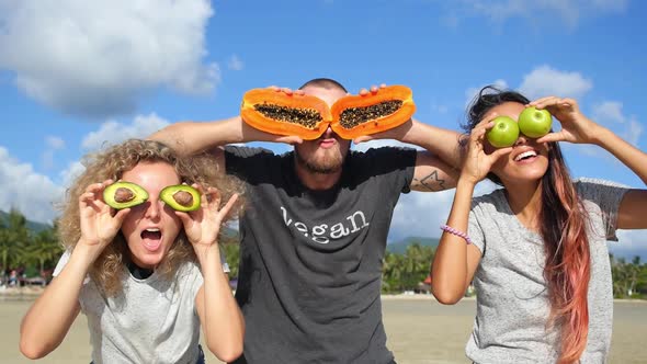 Funny Vegan Friends With Fruits on Eyes Having Fun On Beach in Summer