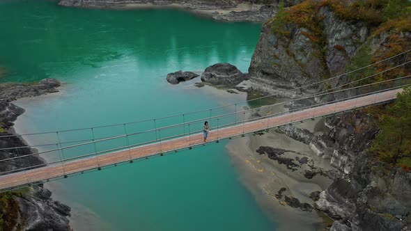 Beautiful Girl Tourist Stands on Hanging Footbridge Across the River