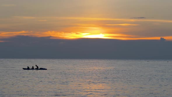 Tourists in a rowboat at colorful orange sunset, silhouettes against the setting sun. SLOW MOTION