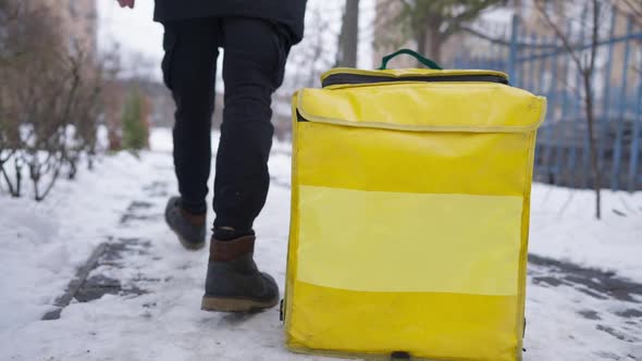 Unrecognizable Man Putting Yellow Thermal Food Delivery Bag on Winter Sidewalk and Leaving