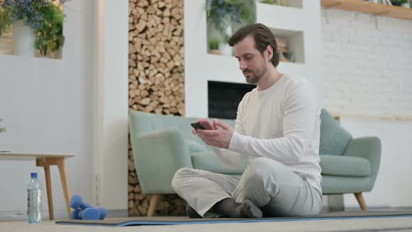 Young Man Using Smartphone on Yoga Mat at Home